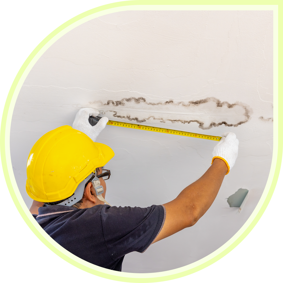 Worker repairing ceiling damage with a measuring tape.