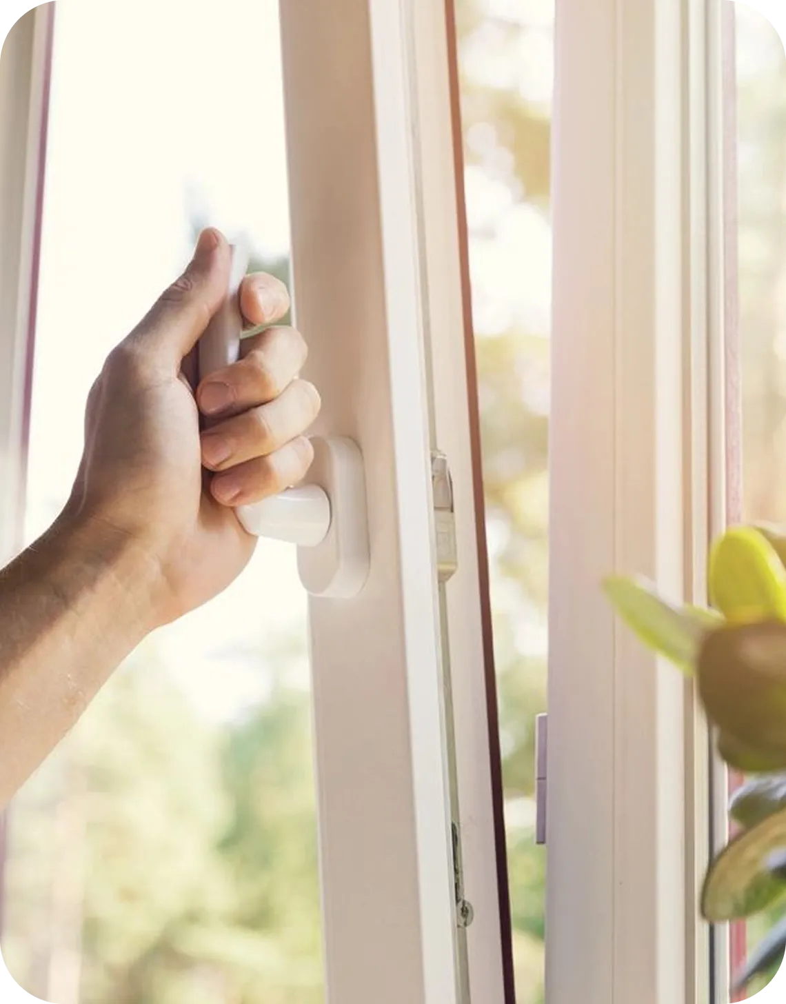 Hand opening a sunlit window indoors.